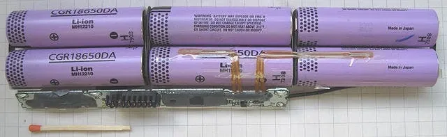 Un pack batterie ouvert montrant des cellules cylindriques CGR18650DA reliées entre elles, avec une allumette à côté pour l’échelle.